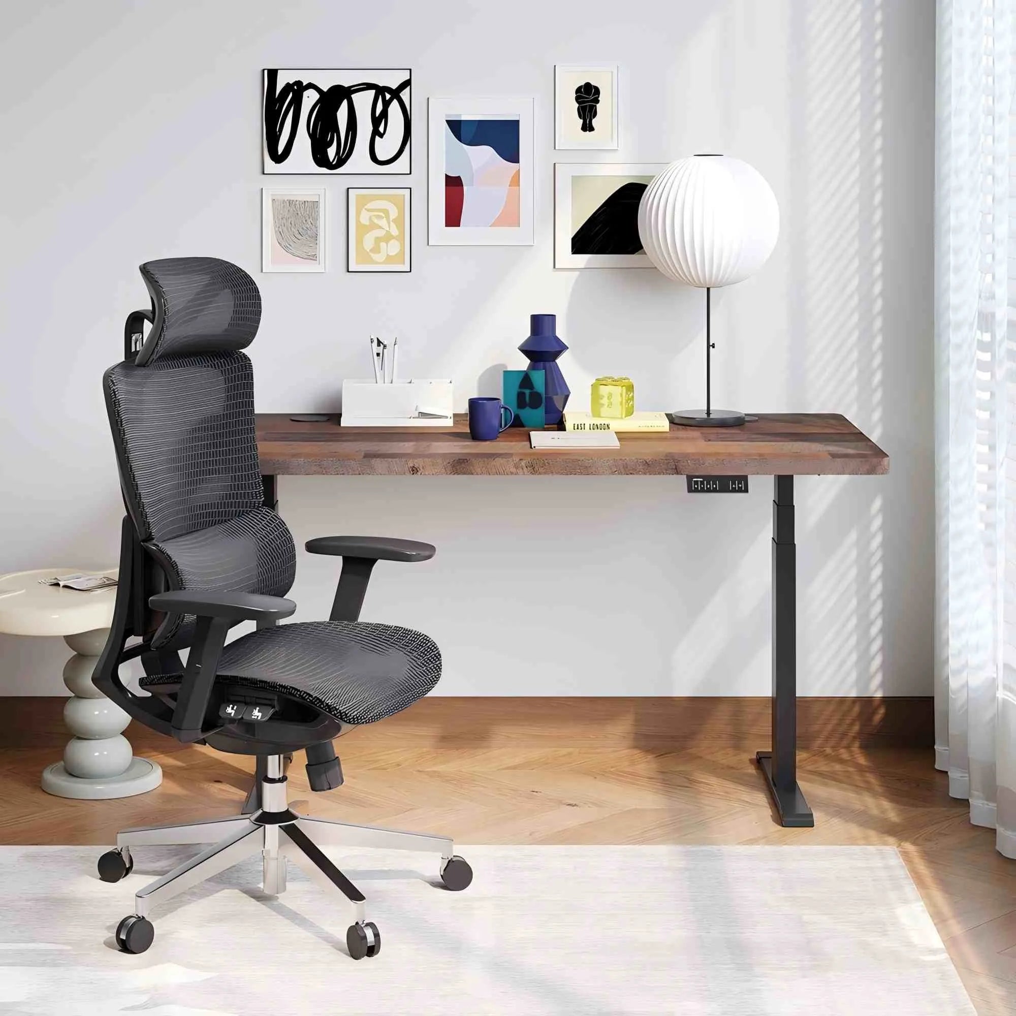 A modern ergonomic office chair in a gray mesh fabric sits next to a wooden height-adjustable desk in a bright, contemporary home office setting.